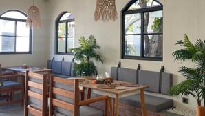 A modern dining area with wooden furniture, a brick accent wall, and large windows. - Ahiva Village (Fulhadhoo)