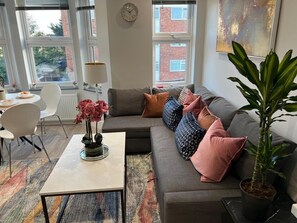 Ein modernes Wohnzimmer mit einem grauen Sofa, bunten Kissen, einem weißen Couchtisch und einem Topf mit Pflanze.