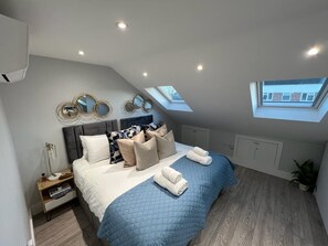 Ein Schlafzimmer mit Bett, Kissen, einem Nachttisch, einer Lampe und einem Oberlicht.