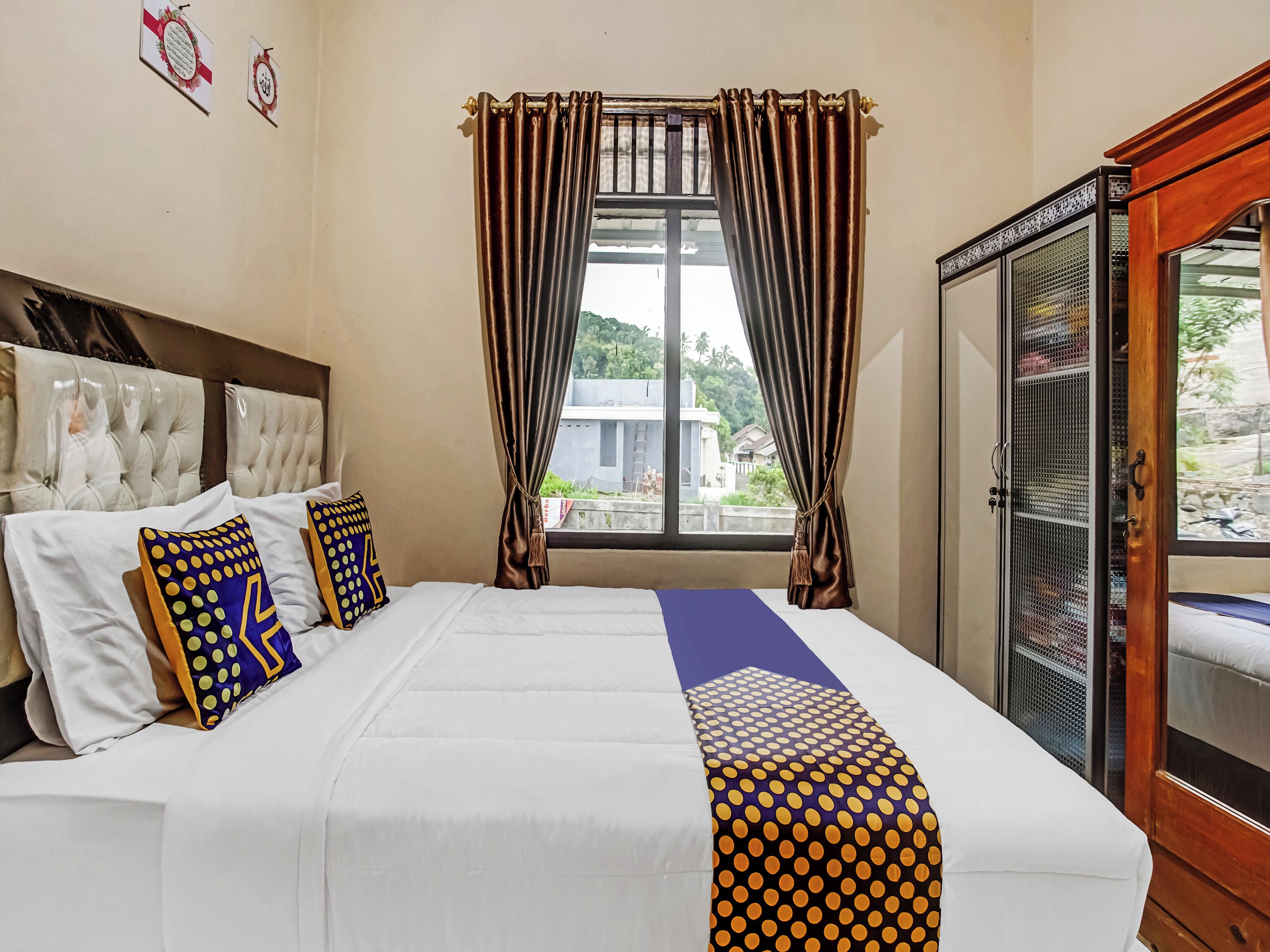 A hotel room with a bed, a window with curtains, a wardrobe, and a view of buildings outside.