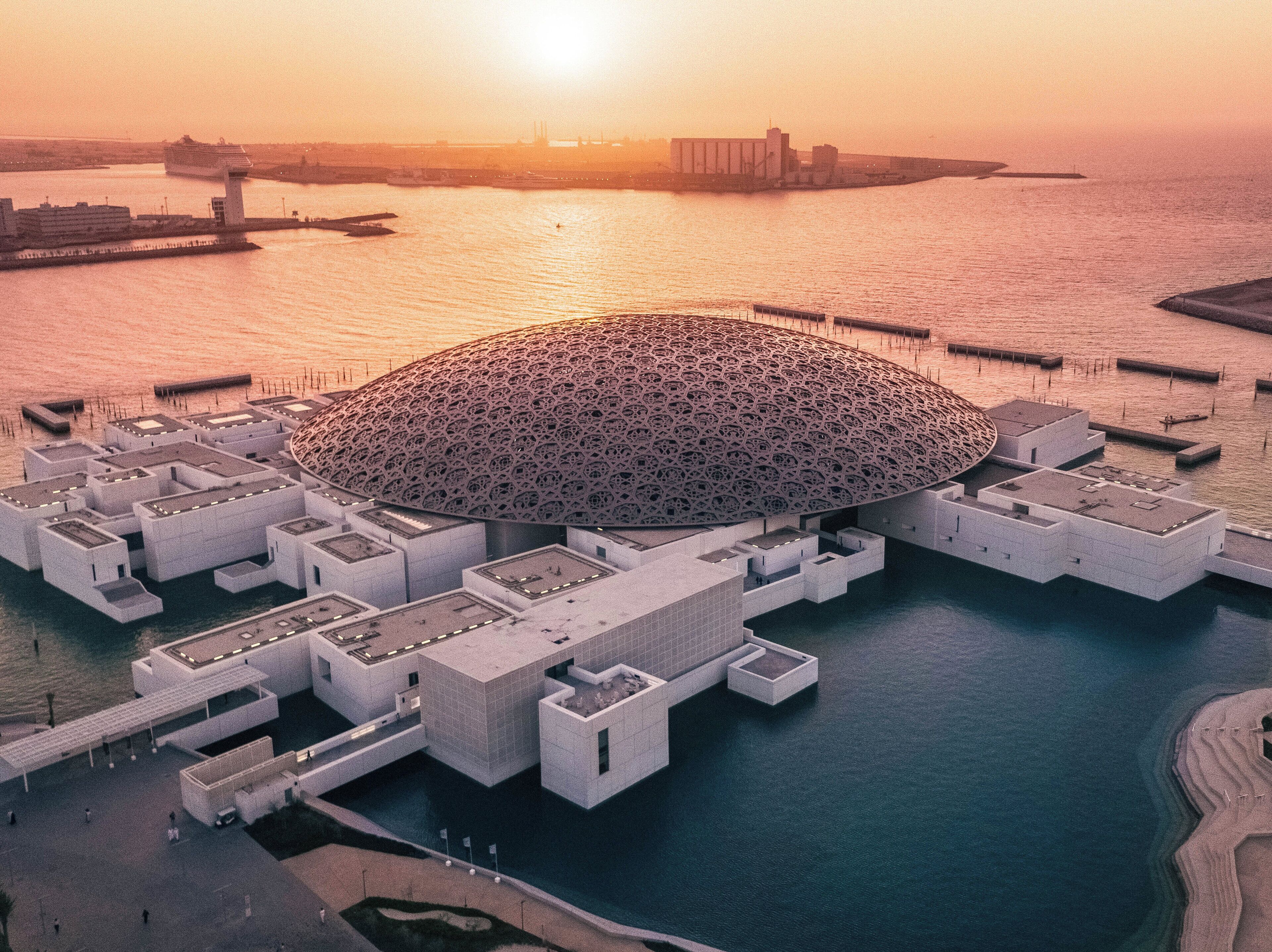 A large, modern building with a distinctive dome structure surrounded by water.