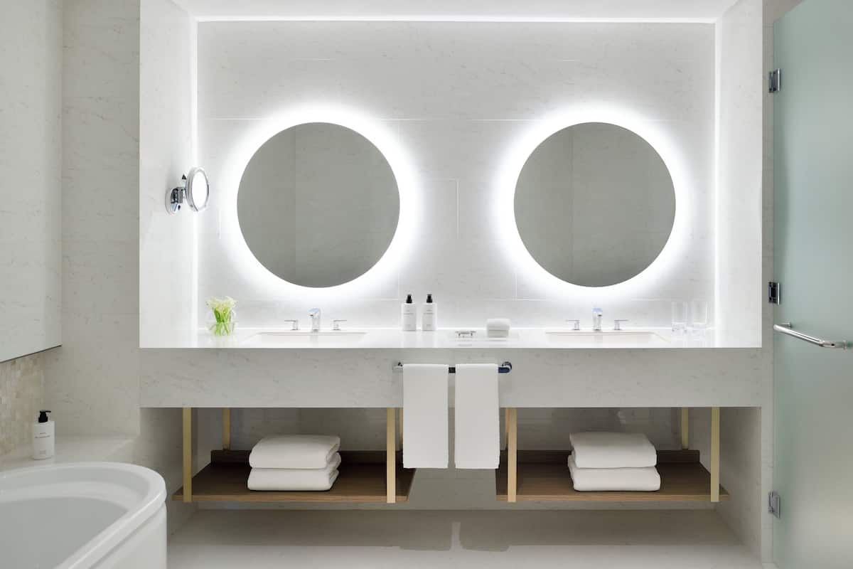 A modern bathroom with a double sink, two large mirrors, and a wooden shelf with towels.