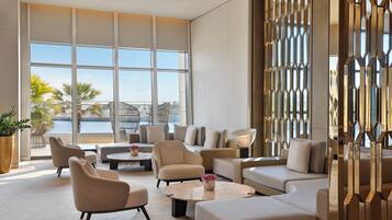 A spacious lounge area with multiple seating options, large windows offering a view of the outdoors, and a decorative metal partition.