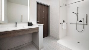 A modern bathroom with a white sink, a wooden vanity, a large mirror, a shower with a handheld showerhead, and a towel rack.