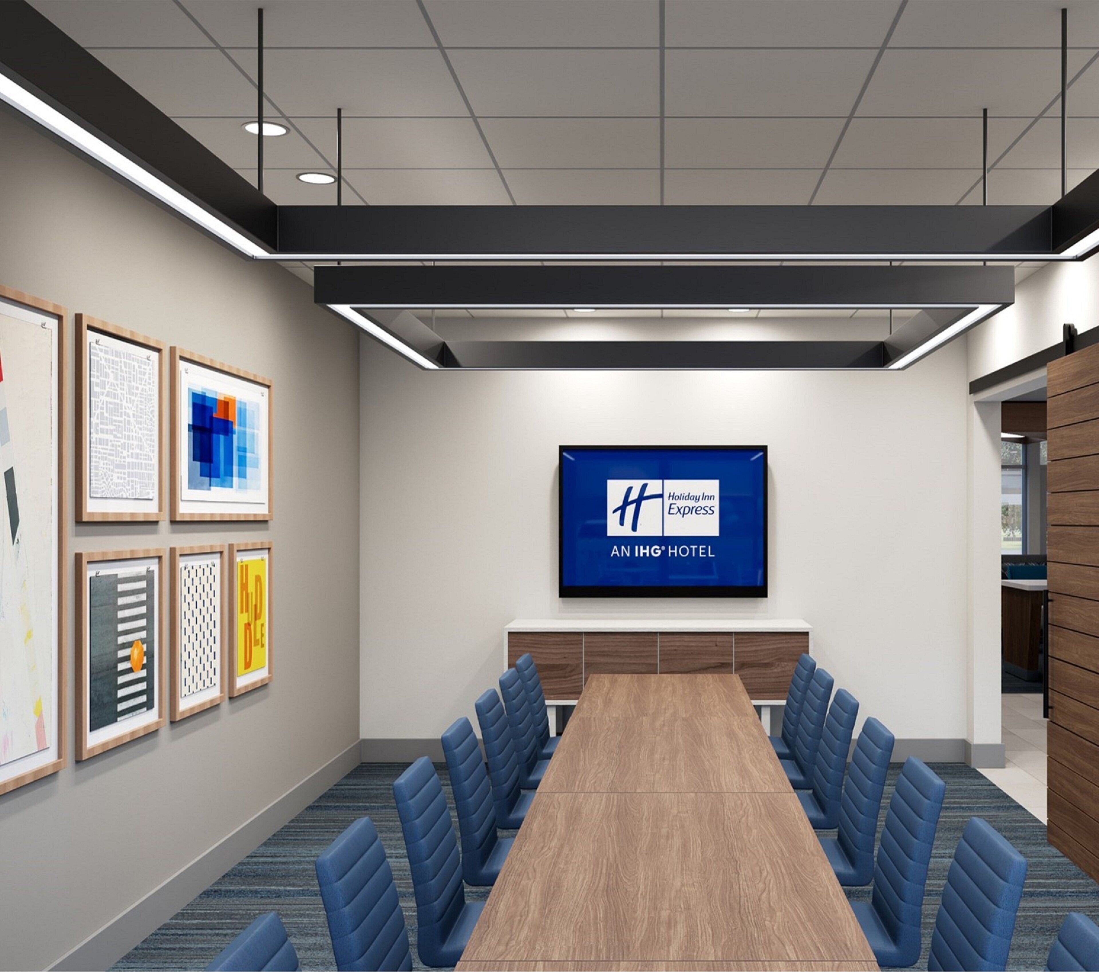 Una sala de conferencias con una mesa larga, sillas azules, obras de arte enmarcadas en las paredes y un cartel de Holiday Inn Express en la pared.