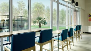 A modern dining area with large windows, blue chairs, and a wooden table. - Holiday Inn Express Jackson - Ridgeland by IHG (Ridgeland)