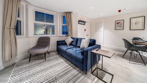 Un salon moderne avec un canapé bleu, un tapis à motifs, une petite table et un coin repas avec des chaises.