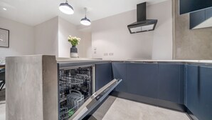 Une cuisine moderne équipée d’un lave-vaisselle, de meubles encastrés et de luminaires suspendus.
