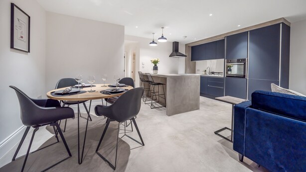 Une cuisine moderne avec des meubles de couleur sombre, un îlot central et un coin repas comprenant une table ronde et des chaises.