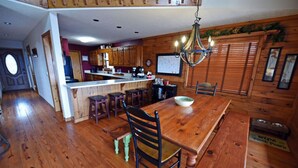 A wooden dining area with a large table and chairs, a kitchen with wooden cabinets, and a chandelier.