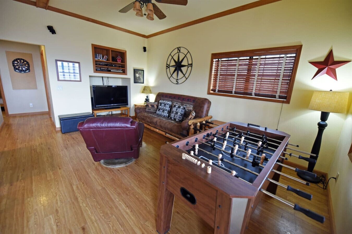 A living room with a foosball table, a leather sofa, a television, and a dartboard.