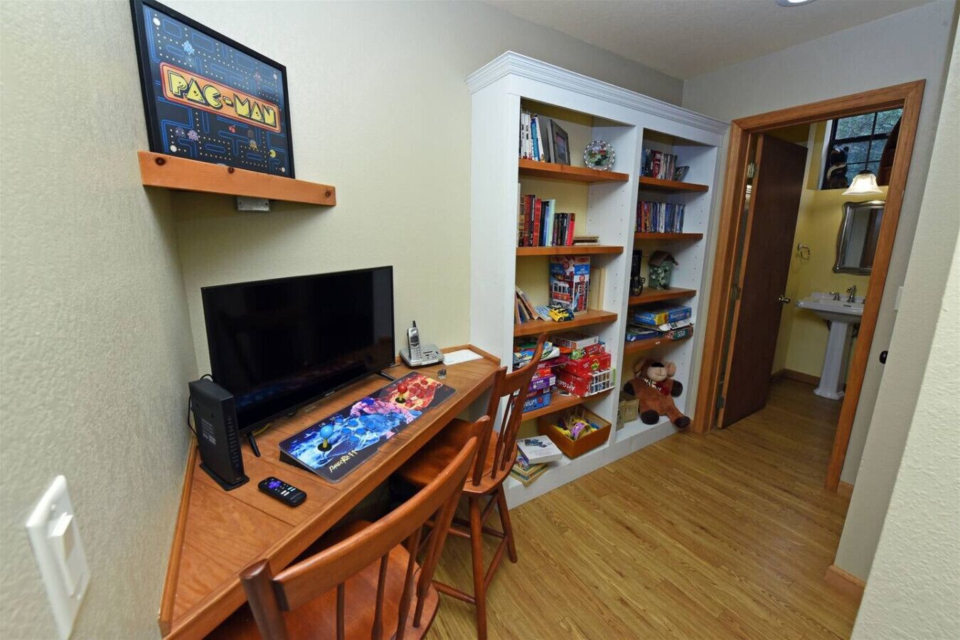 A room with a wooden desk, a television, and a bookshelf filled with books and toys.