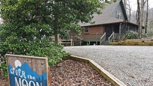 A wooden sign with the text "OVER the MOON" in front of a building with a gravel driveway and a wooden fence.