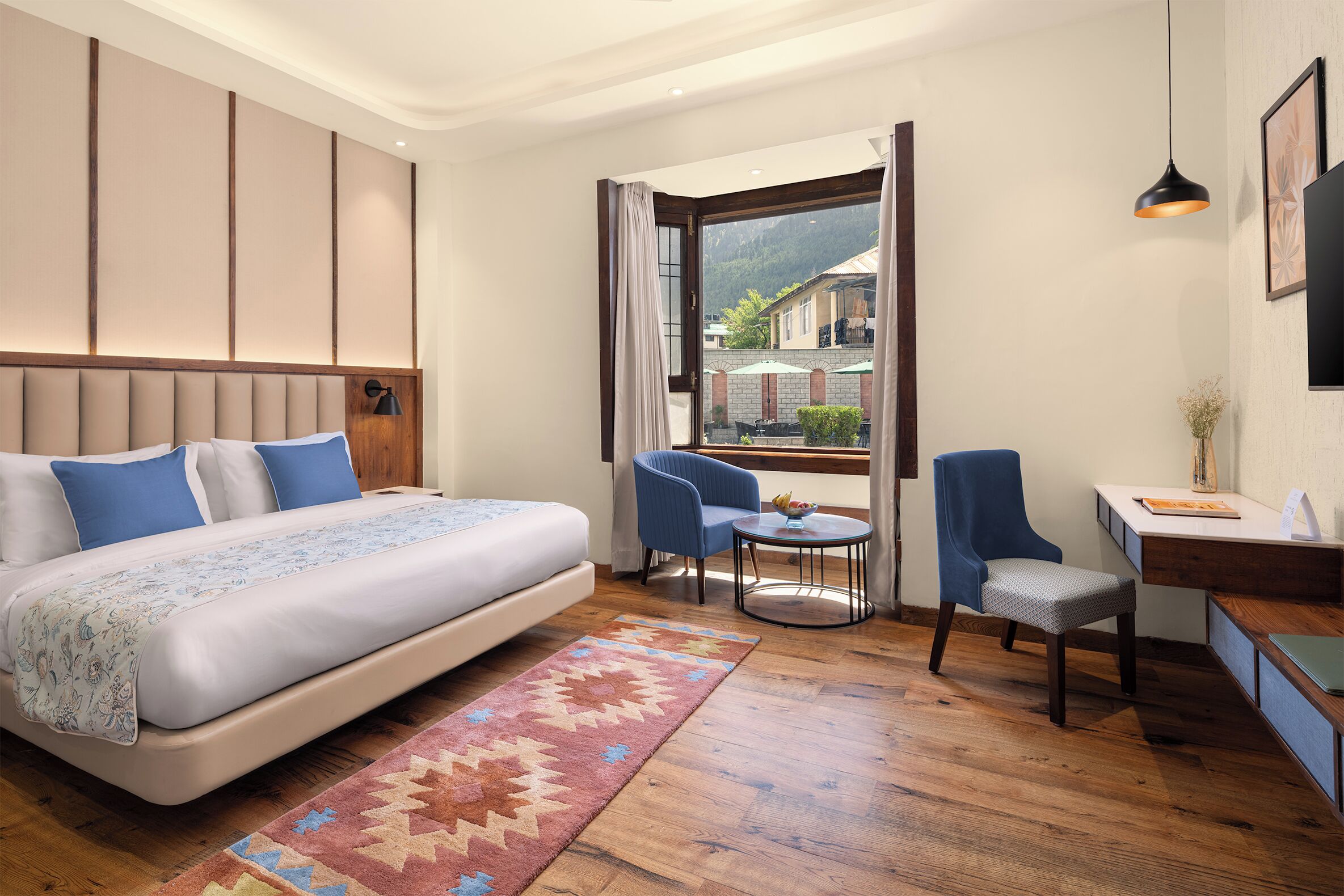 A hotel room with a bed, a desk, a chair, a small table, and a view of the outside.