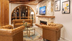A living room with leather sofas, a glass coffee table, a fireplace, and a stone wall with artwork. - Kanishka, Manali- AM Hotel Kollection (Manali)
