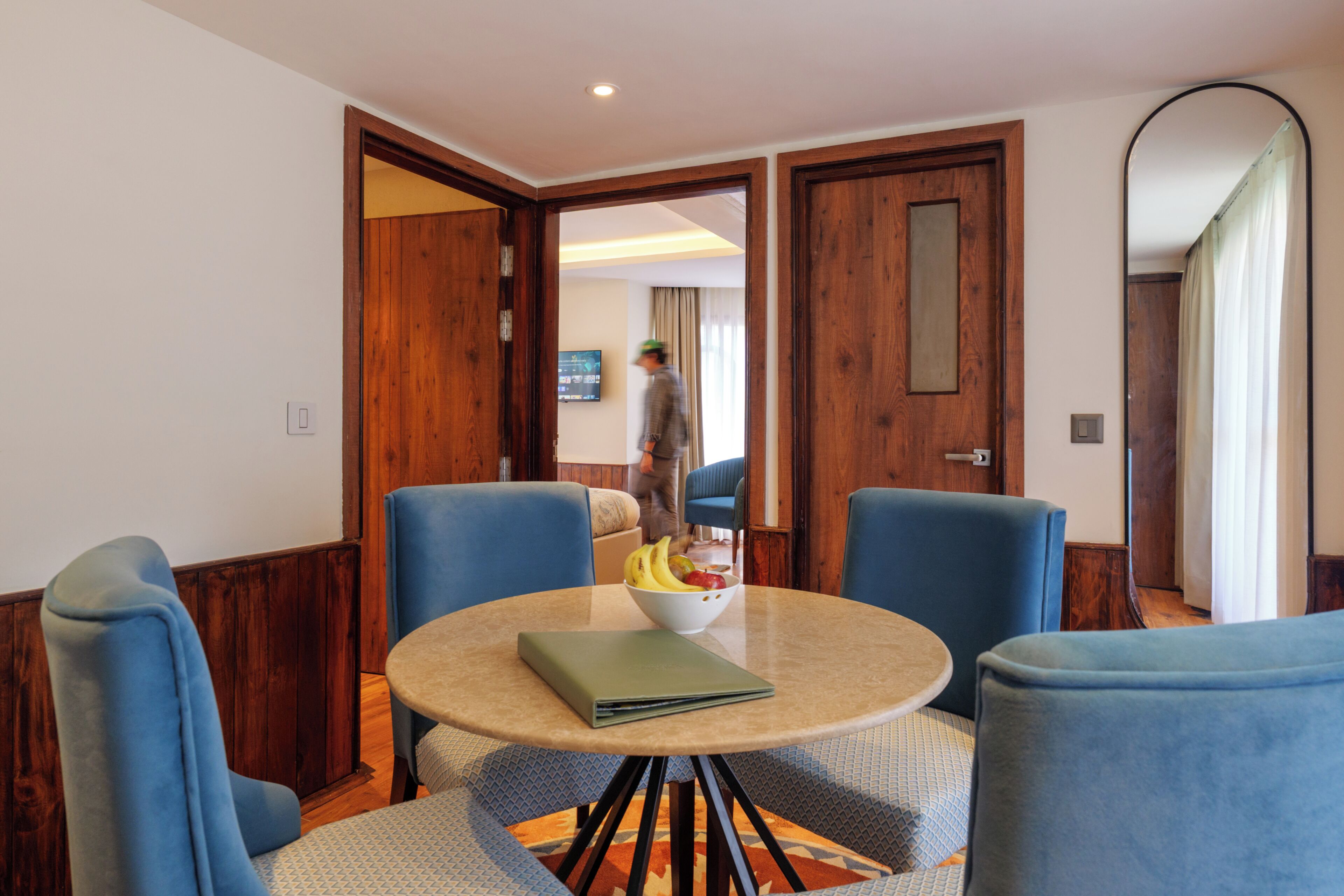 A room with a round table, blue chairs, a bowl of fruit, and a green folder.