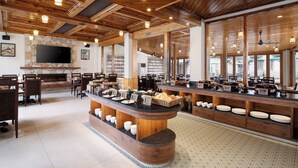 A restaurant with a stone fireplace, wooden ceiling, and a buffet counter with plates and baskets. - Kanishka, Manali- AM Hotel Kollection (Manali)