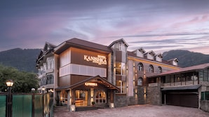 A hotel with a prominent sign, a brick facade, and a mountainous backdrop. - Kanishka, Manali- AM Hotel Kollection (Manali)