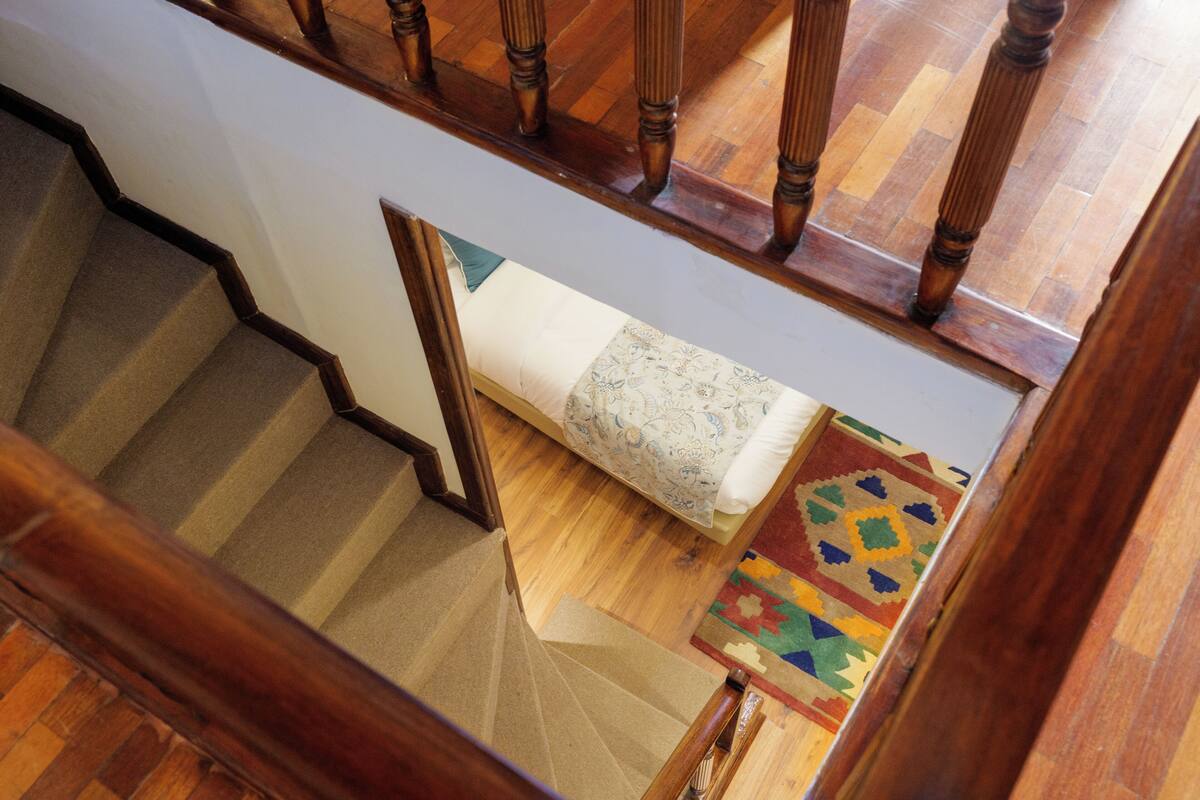 A staircase with wooden railings, carpeted steps, a bed with a patterned bedspread, and a colorful rug on the floor.
