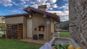 Une cuisine extérieure rustique, dotée d’un four à bois, d’un mur en pierre et d’une table en bois sur laquelle sont disposés des légumes.