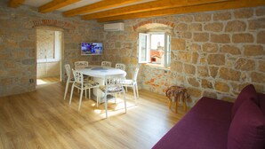 A room with a stone wall, wooden beams, a dining table with chairs, a purple sofa, and a TV on the wall. - Villa Veli Varos, 4 bedrooms, near Diocletian pallace, Split old town (Split)