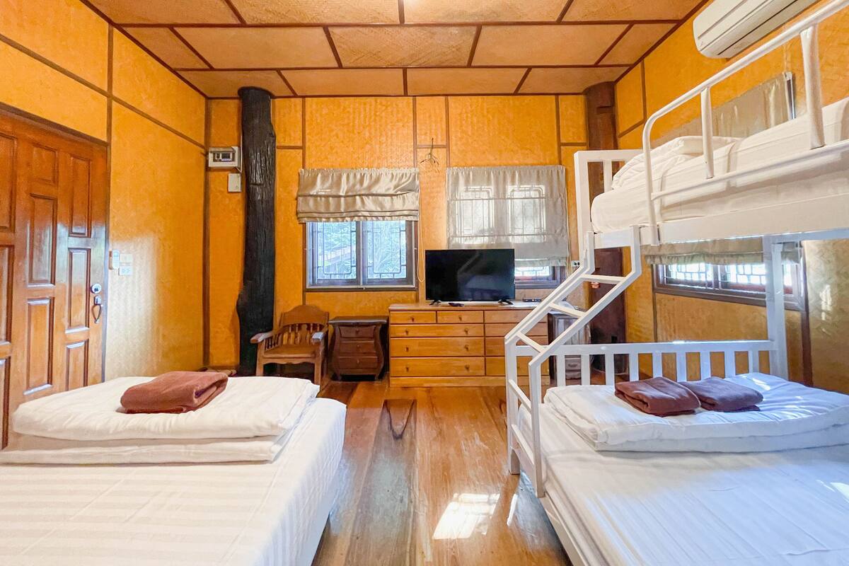 A room with two bunk beds, a television on a dresser, a window with curtains, and a wooden door.