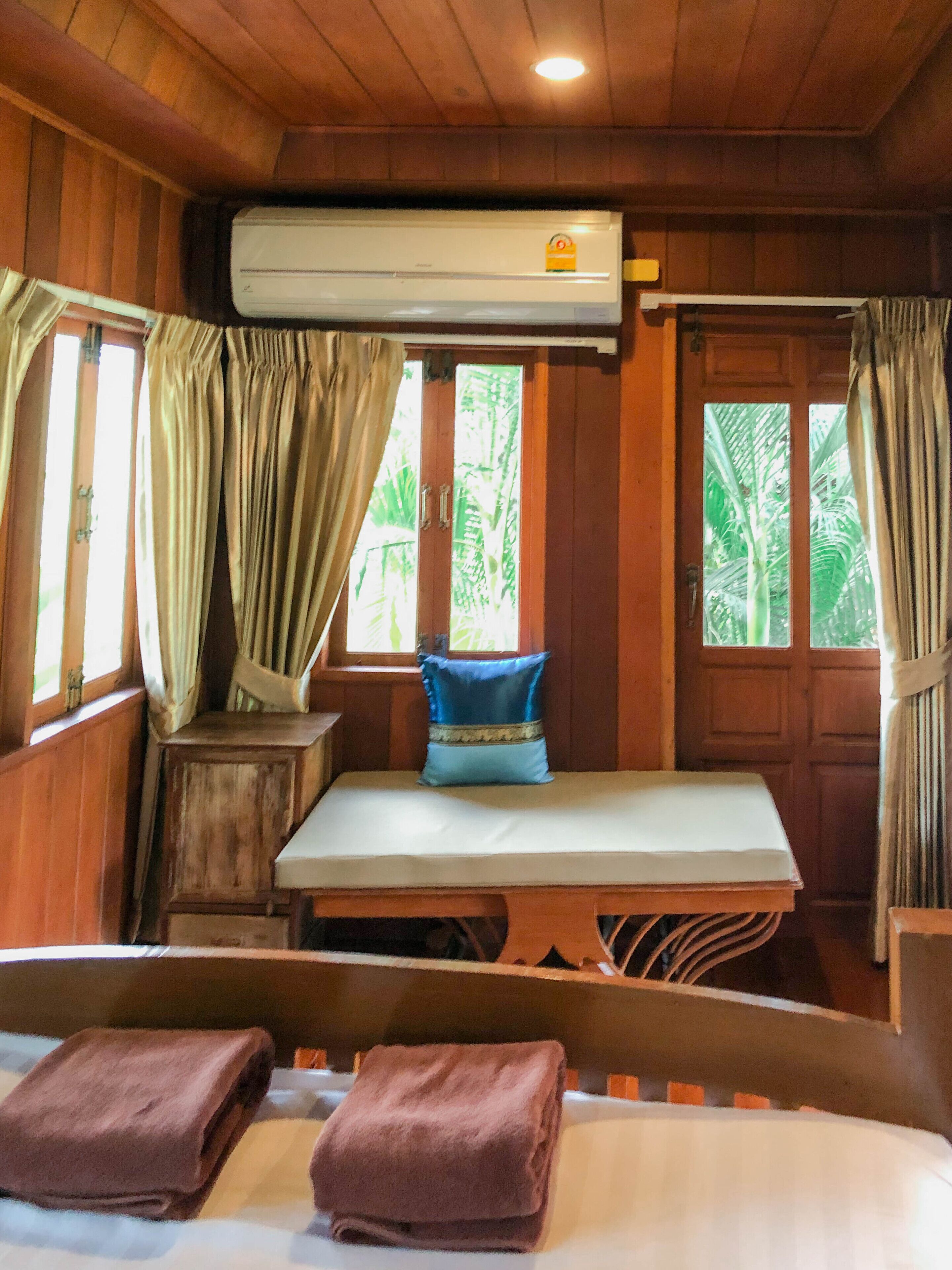 Ein Zimmer mit Holzboden, einem Bett, einem Tisch mit Kissen und einer Klimaanlage.