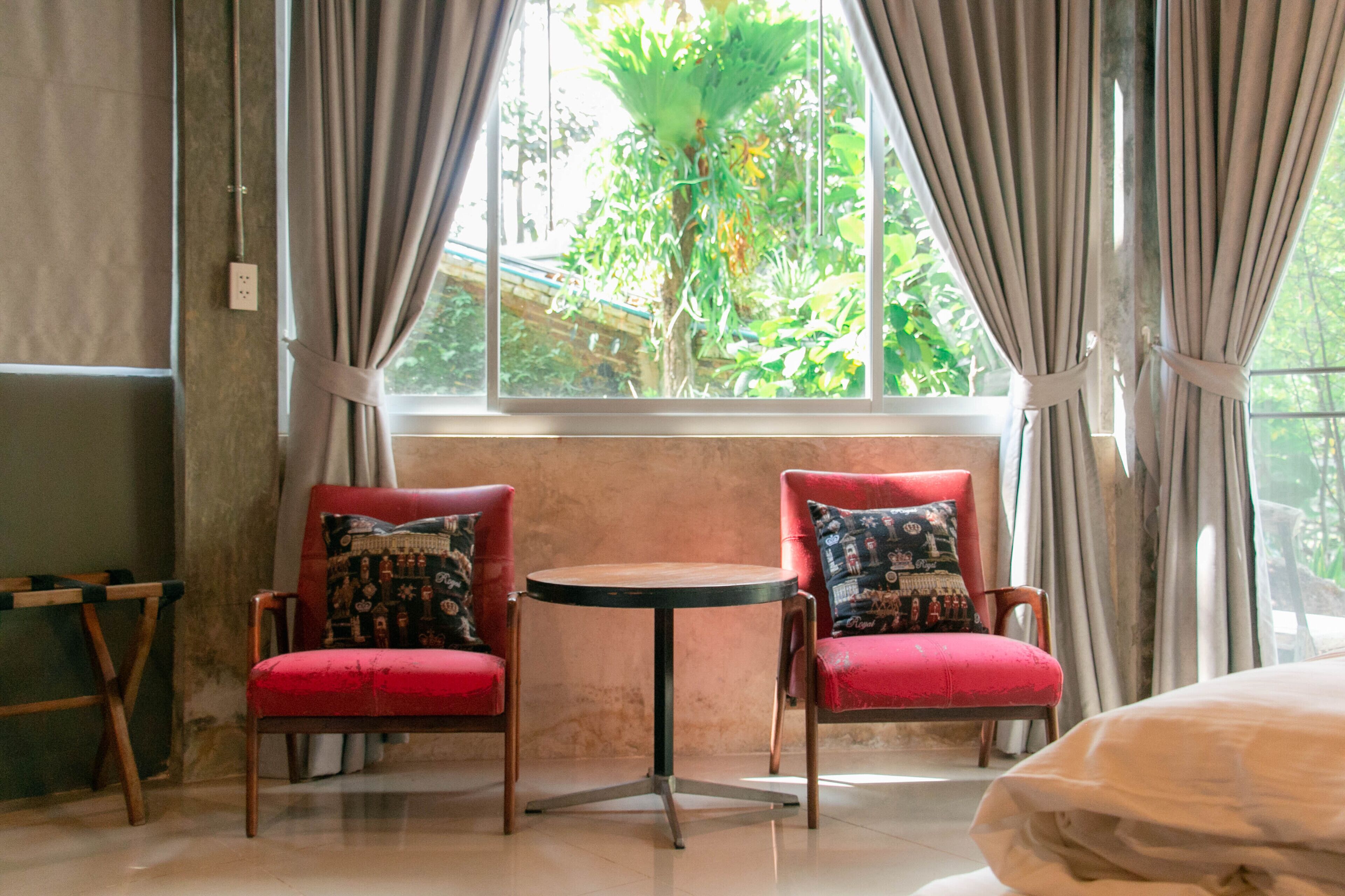 A room with two red chairs, a small round table, and a window with curtains.