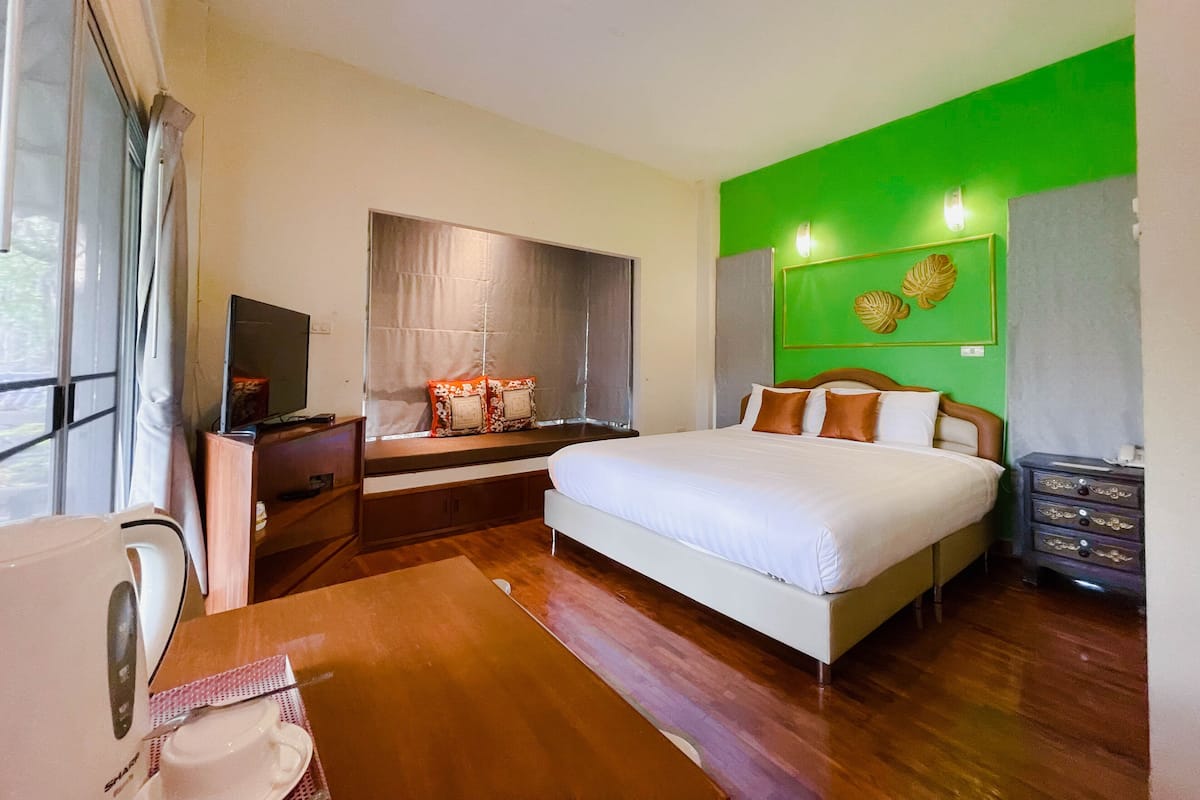 A hotel room with a large bed, a television, a desk with a kettle, and a green accent wall.