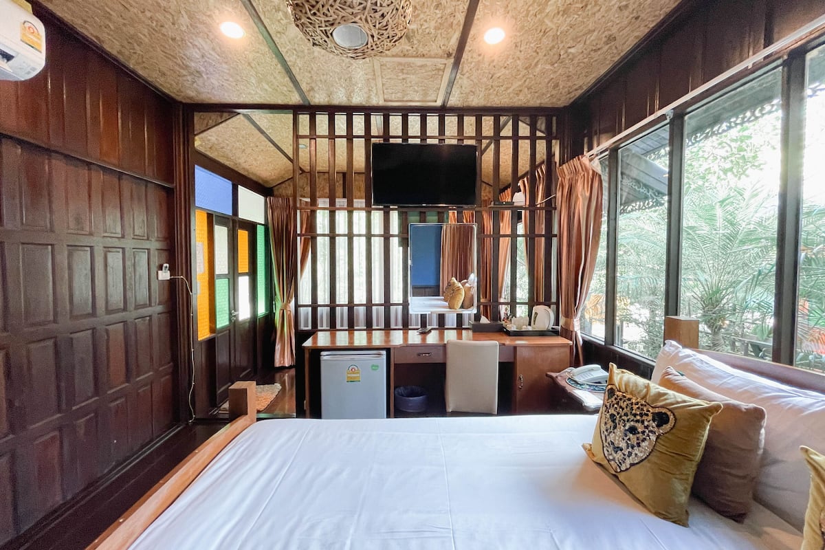 A room with a bed, desk, and a television. There is a window with curtains and a view of trees.