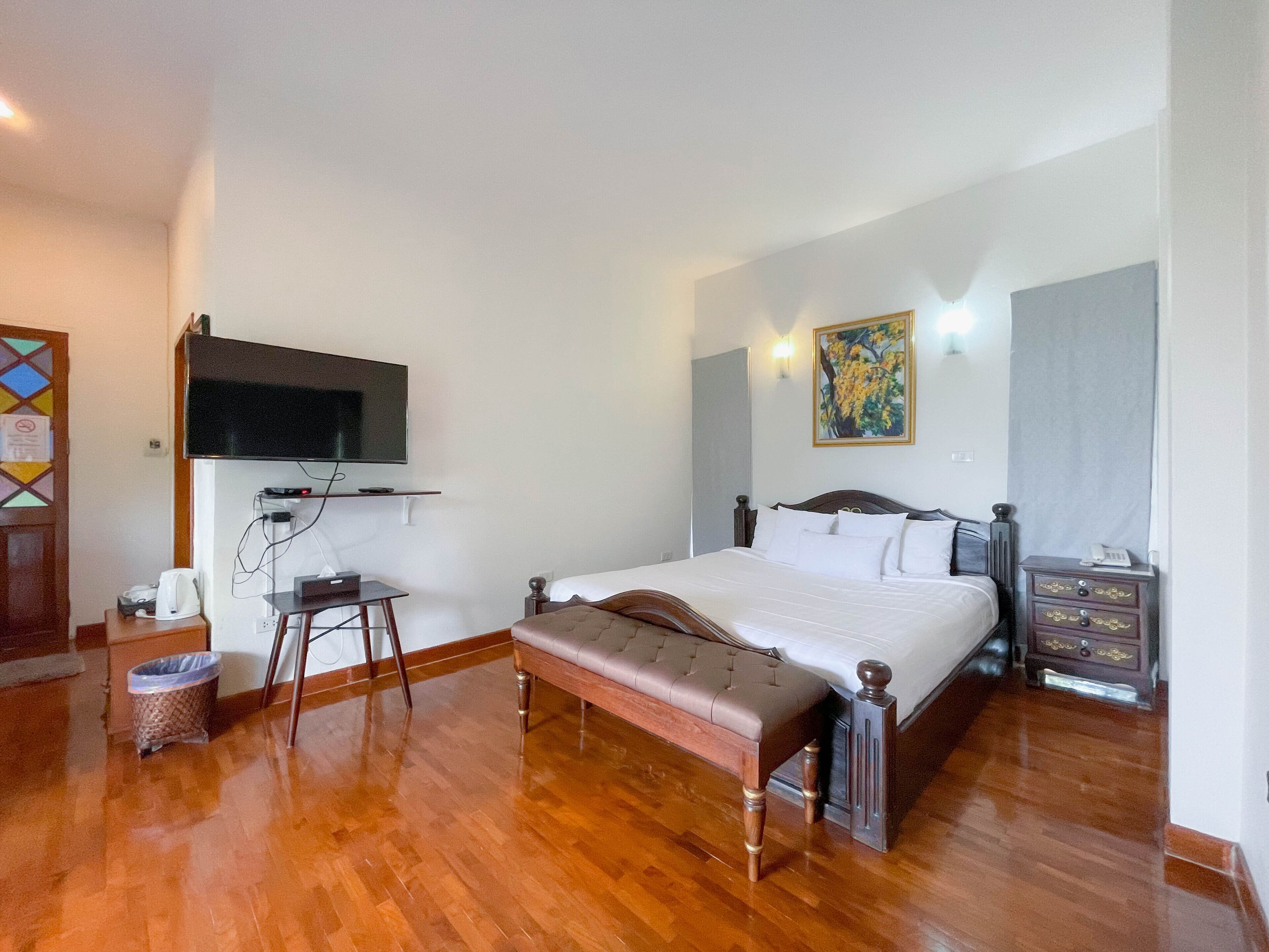 Habitación de hotel con piso de madera, cama con cabecera, una banca, escritorio con computadora, televisor montado en la pared y un cuadro en la pared.