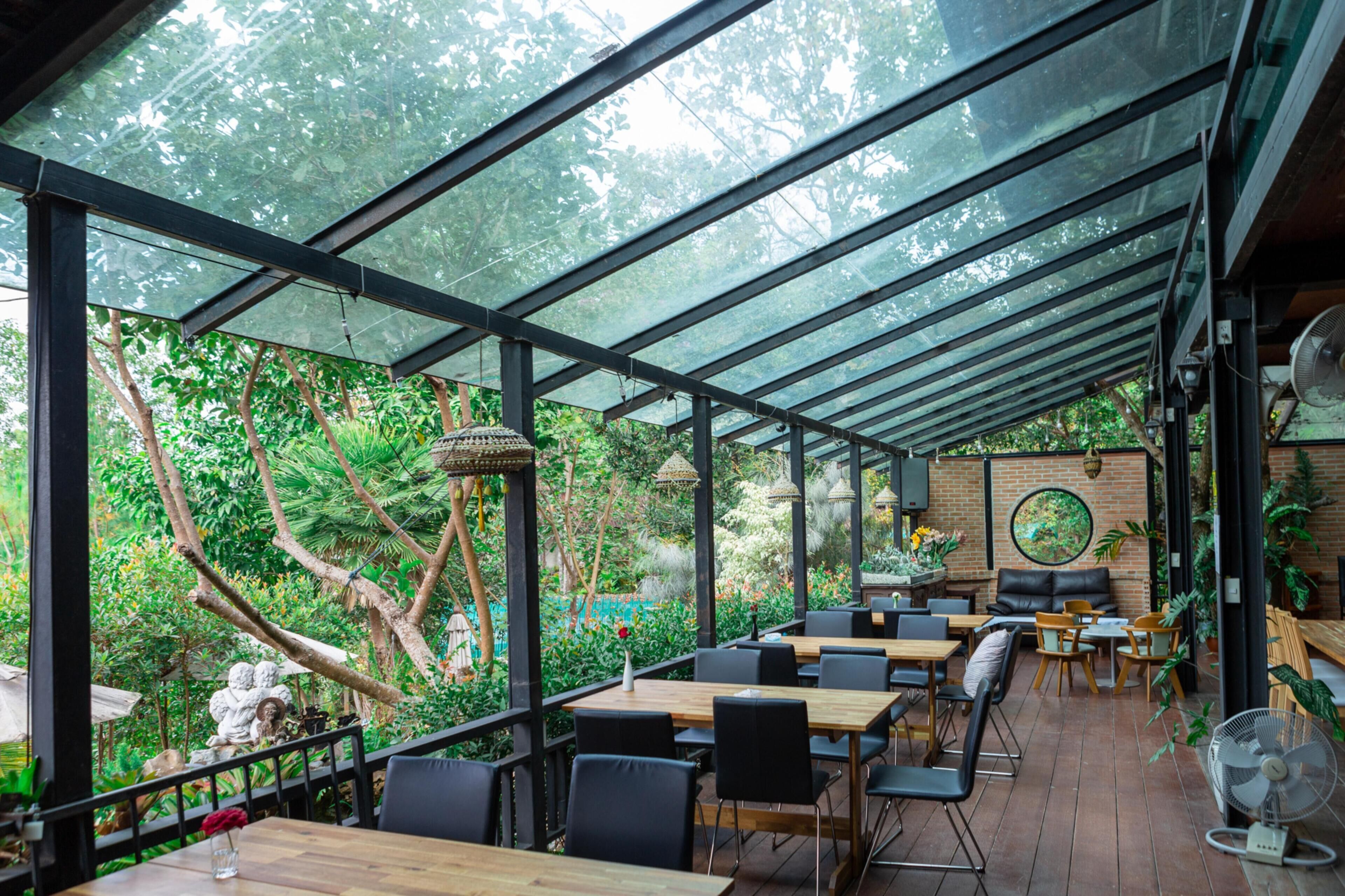 An indoor garden restaurant with glass walls, wooden tables, and black chairs.