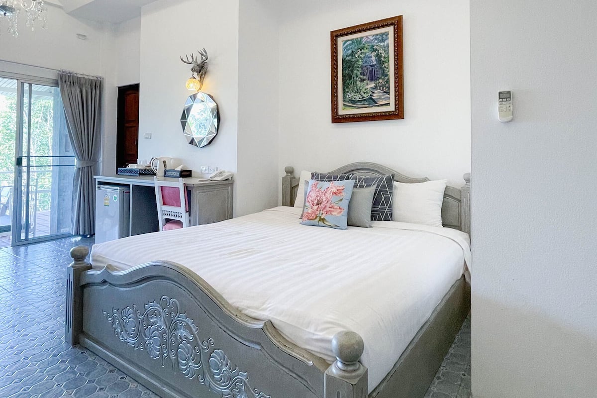 A bedroom with a large bed, a chandelier, a painting, and a desk with a telephone.