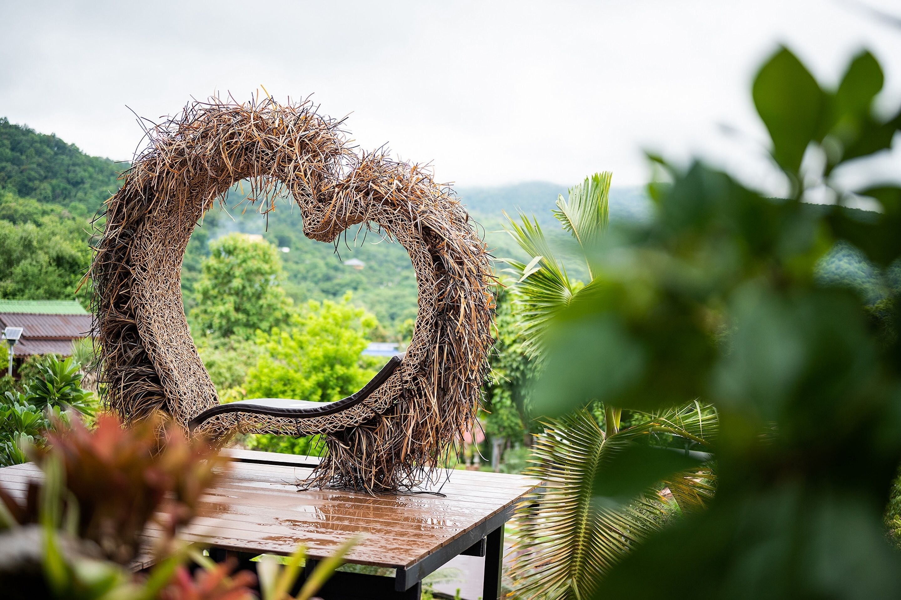 Une structure en forme de cœur, faite de matériaux naturels, peut-être de paille ou de roseaux, placée sur une plateforme en bois.