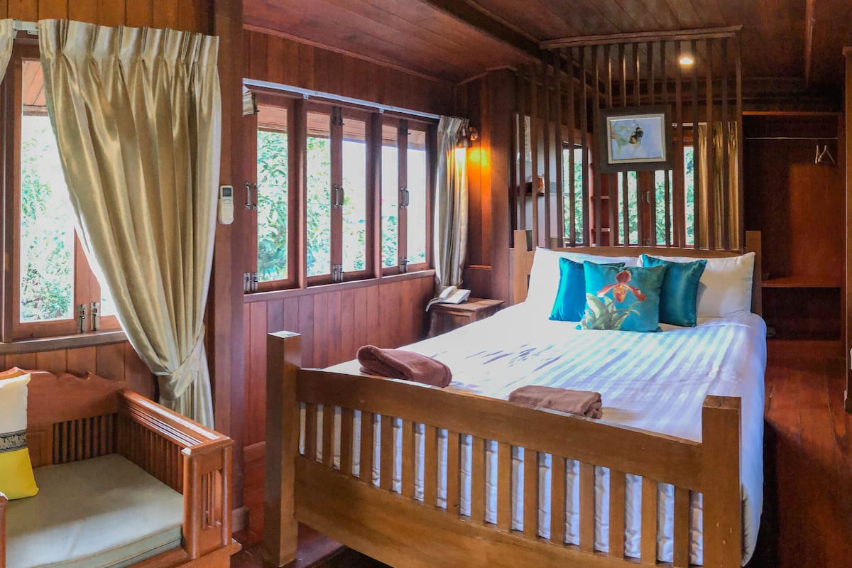 A wooden room with a bed, a bedside table, a chair, and a window with curtains.