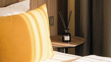 Une chambre d’hôtel comprenant un lit, une table de chevet, une lampe fixée au mur et une table sur laquelle se trouve un diffuseur d’ambiance à bâtonnets.