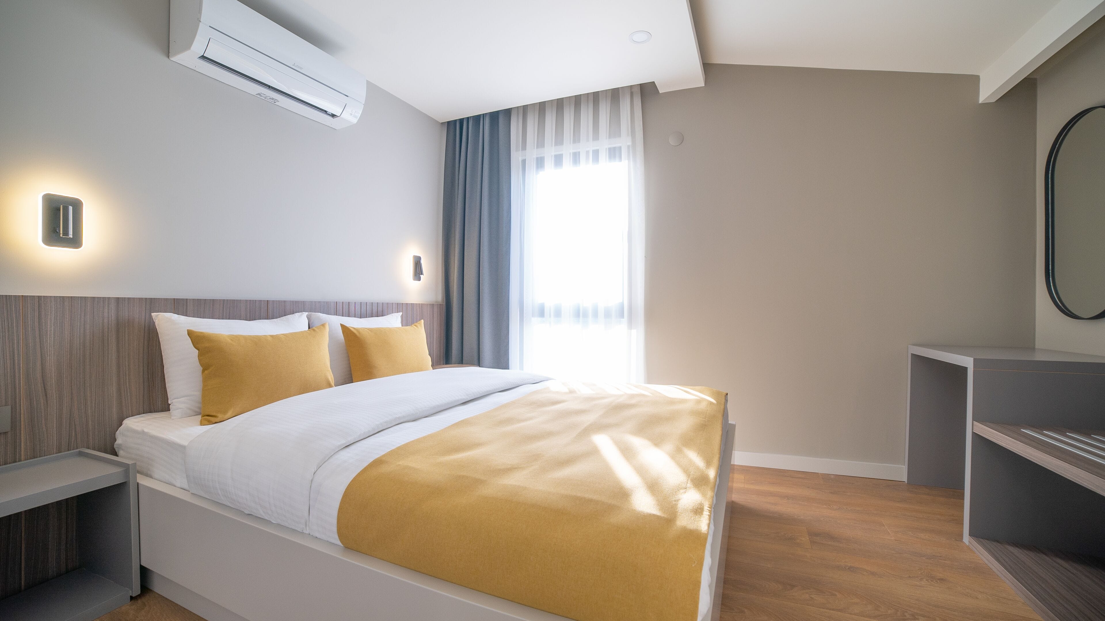 Ein modernes Hotelzimmer mit Bett, Nachttischen, Klimaanlage, Schreibtisch und Spiegel.