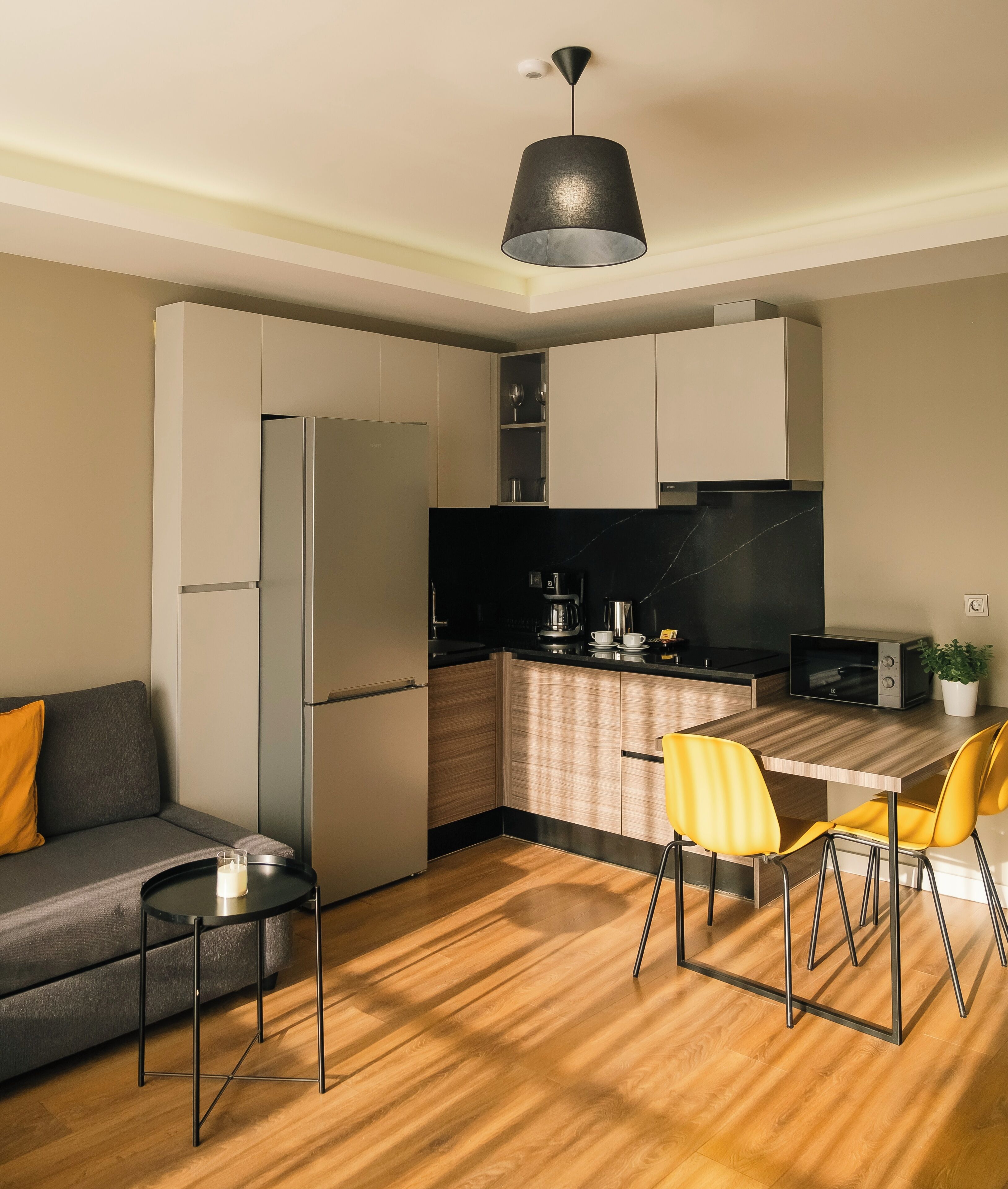 Una cocina moderna con refrigerador empotrado, cafetera y comedor con mesa de madera y sillas amarillas.