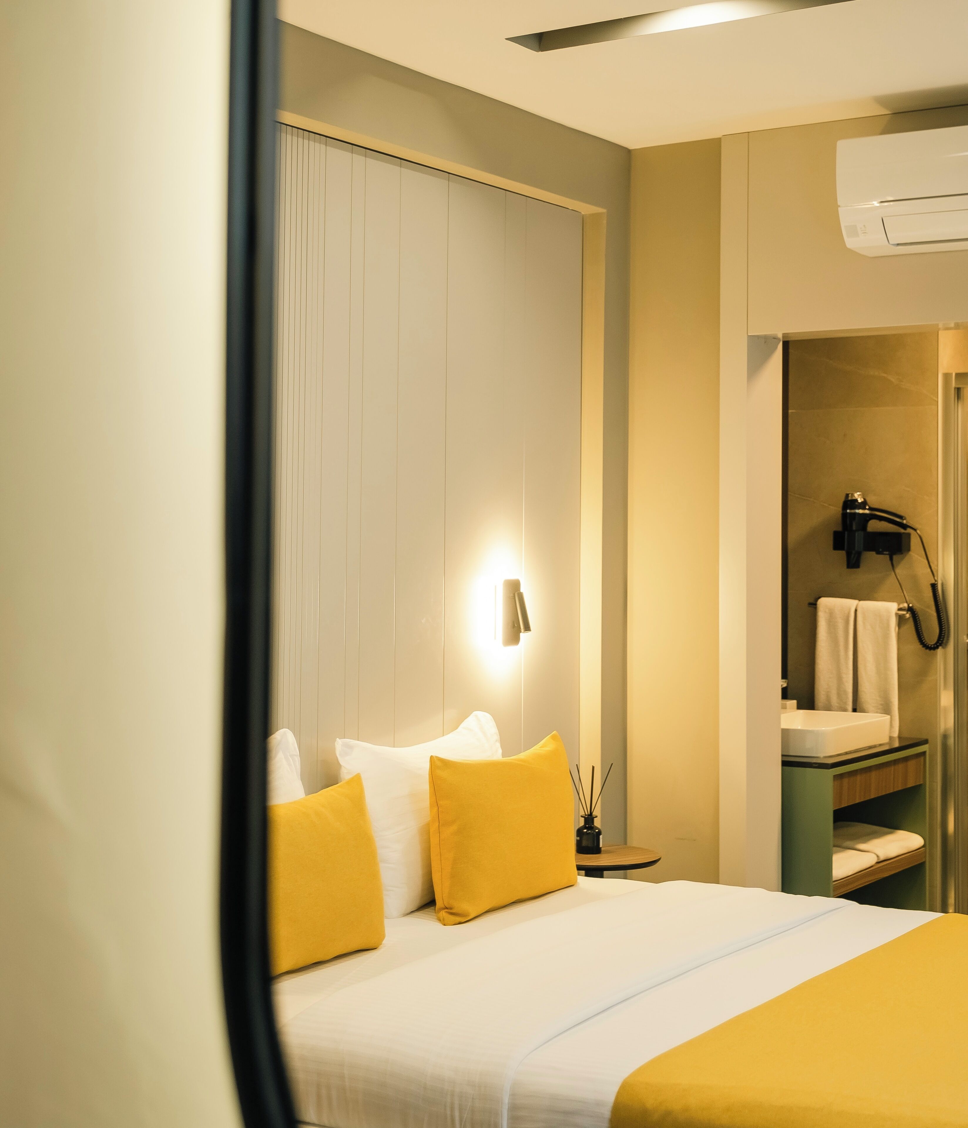 A hotel room with a bed, a nightstand, a wall-mounted lamp, a hairdryer, and a mirror.