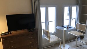 A room with a TV on a wooden cabinet, a round table with two chairs, and large windows. - Paris Studio atypique - Place des victoires (Paris)