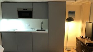 A compact kitchen with grey cabinets, a built-in microwave, a sink, and a small window. - Paris Studio atypique - Place des victoires (Paris)