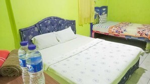 Quarto com duas camas, uma com colcha florida e outra com padrão listrado. Há duas garrafas de água sobre uma mesa.