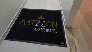 Um corredor com um tapete preto na entrada, com a inscrição "MATZON APART HOTEL".