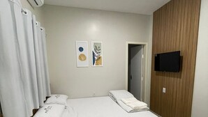 Quarto de hotel com uma cama, uma televisão fixada na parede e um aparelho de ar condicionado.