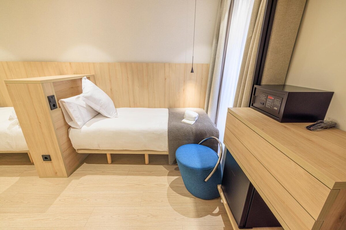 Quarto de hotel pequeno com cama, escrivaninha, cadeira e micro-ondas.