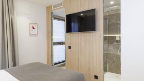 A modern hotel room with a large bed, a flat-screen TV mounted on the wall, a shower area, and a wooden panel design. - Inn Boutique León (León)
