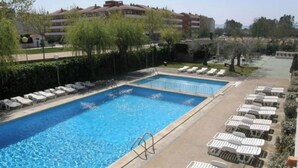 Piscina rectangular con dos zonas separadas, rodeada de sillas de descanso y un muro bajo.