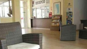 Un área de recepción con muebles de mimbre, un mostrador de recepción y un atril para revistas.