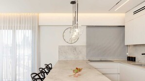 Une cuisine moderne dotée d’un îlot en marbre, de tabourets de bar noirs et de luminaires suspendus.