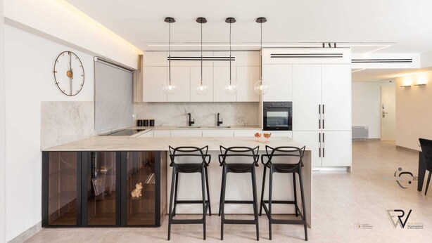 Une cuisine moderne dotée d’un îlot central, de tabourets de bar, de luminaires suspendus et d’une horloge au mur.